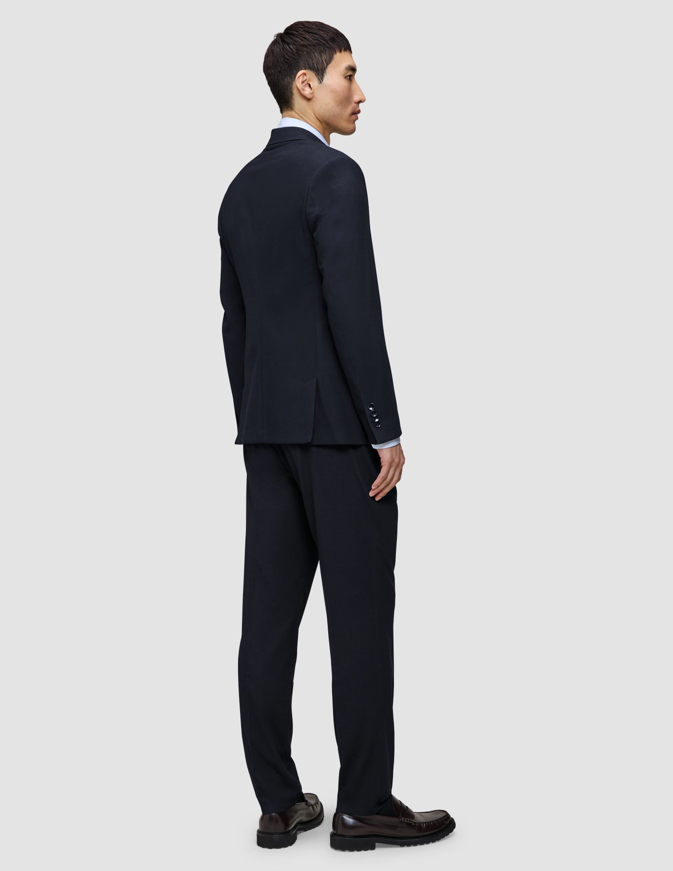 Ein Mann, von hinten gesehen, der einen Motion Blazer Slim in Mitternachtsblau und eine dazu passende Hose aus einem 360°-Stretch-Material trägt, kombiniert mit dunklen Loafern.